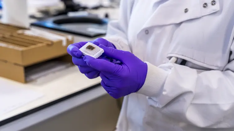 A scientist in a lab coat holds a sample in a laboratory setting.