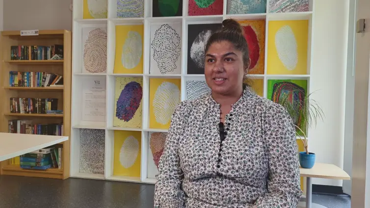 Fozia speaking off camera to Mon, in front of a colourful background with drawings representing thumb prints done in with different artistic methods.