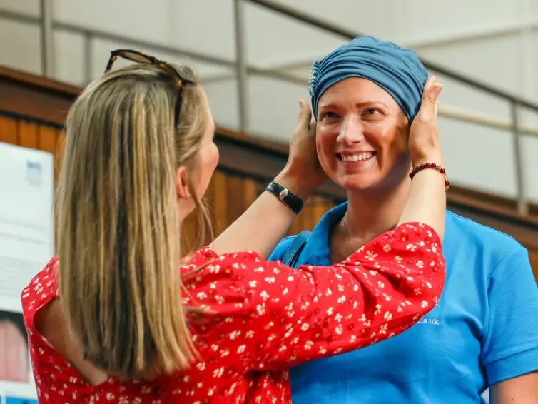 two women smiling, with one woman in red top adjusting the other's blue headwear.