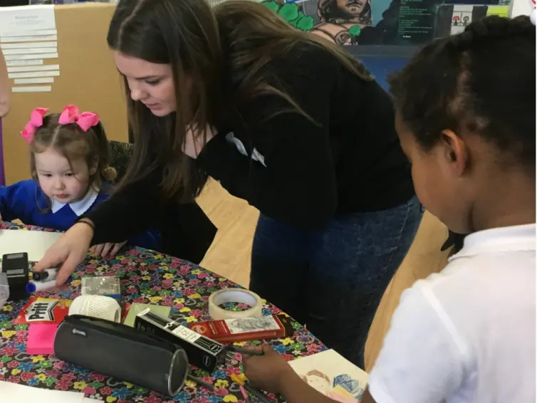 Two children at a table doing art with adult helping.