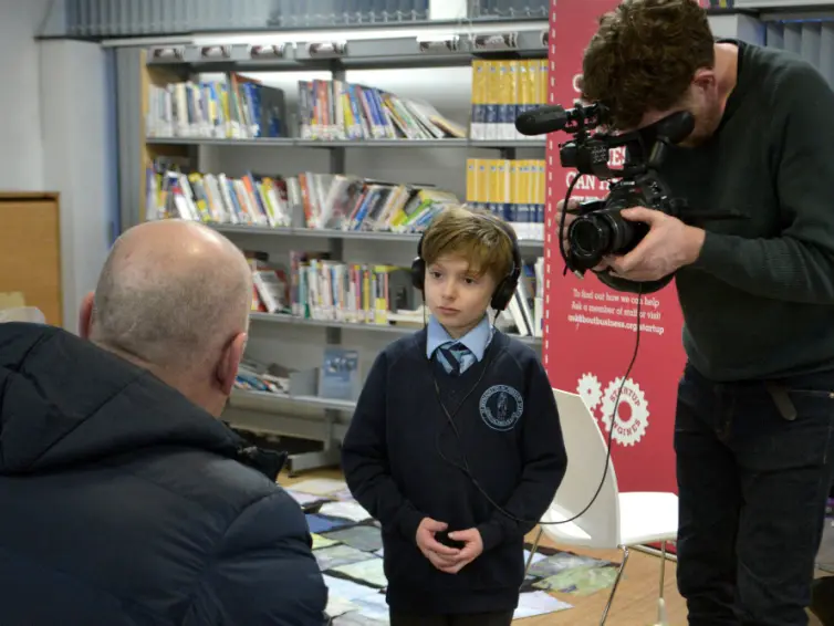 Child interviewing a person with another person filming the interview.