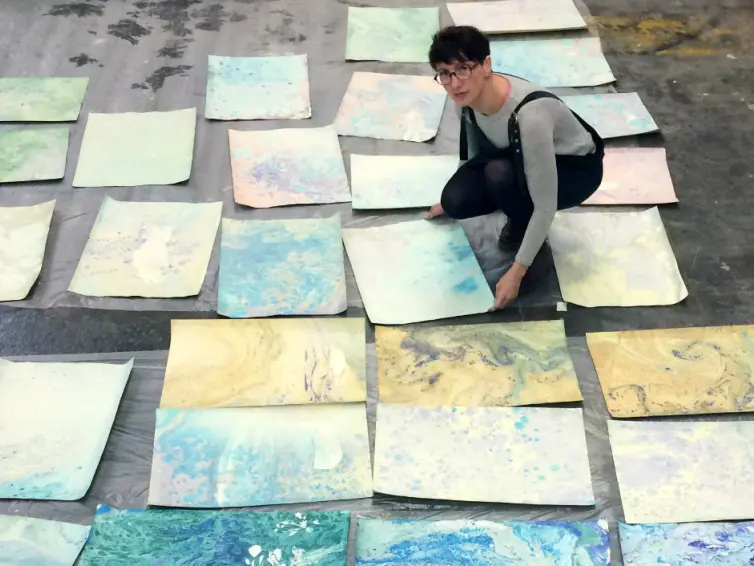 Woman with marbled paper spread out on the floor.