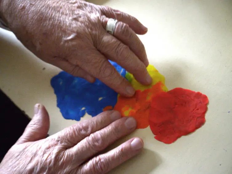 Image of two hands squashing red, orange, yellow and blue playdough.