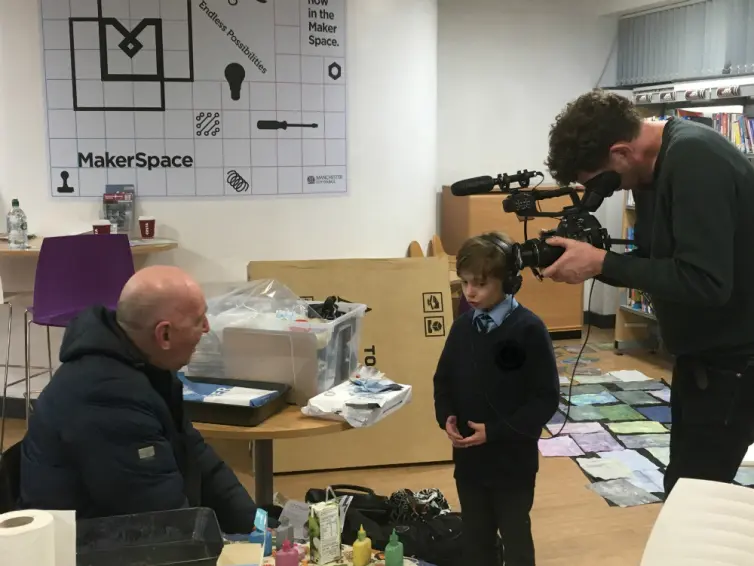 Image of young boy interviewing a man with a man filming the interview.