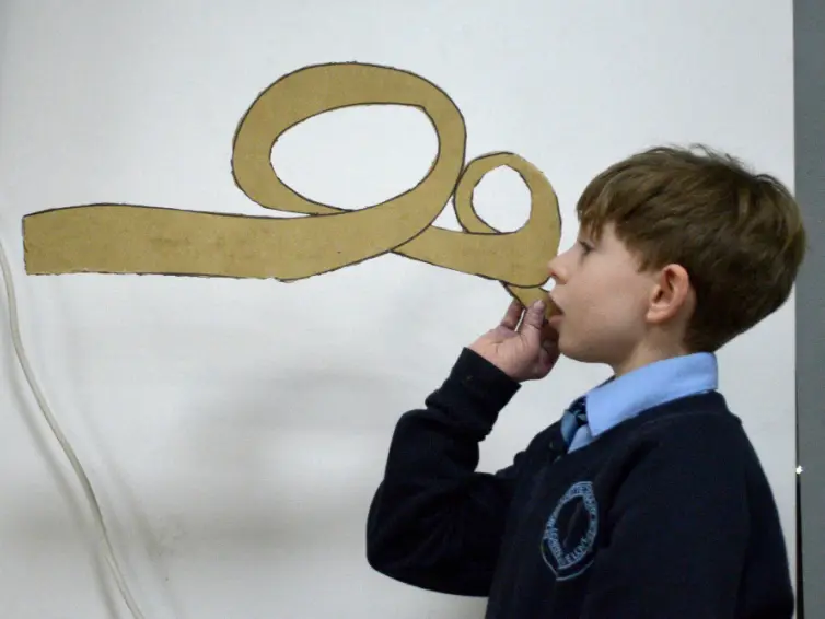 Image of a young boy holding a spital-shaped piece of cardboard up to his mouth.