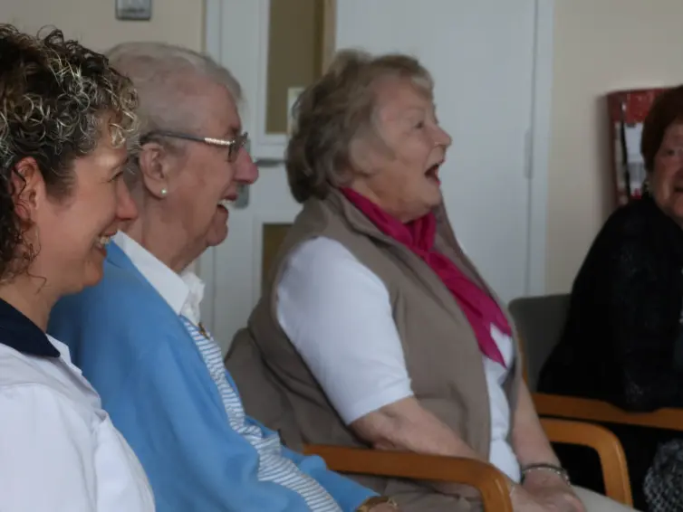 Image of four women sitting down, singing and laughing including a physiotherapist in uniform.