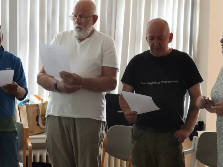 Image of three men and one woman standing and singing with song sheets in hands.