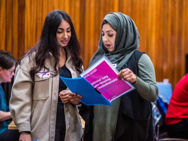 Two people reading a booklet in a busy room.