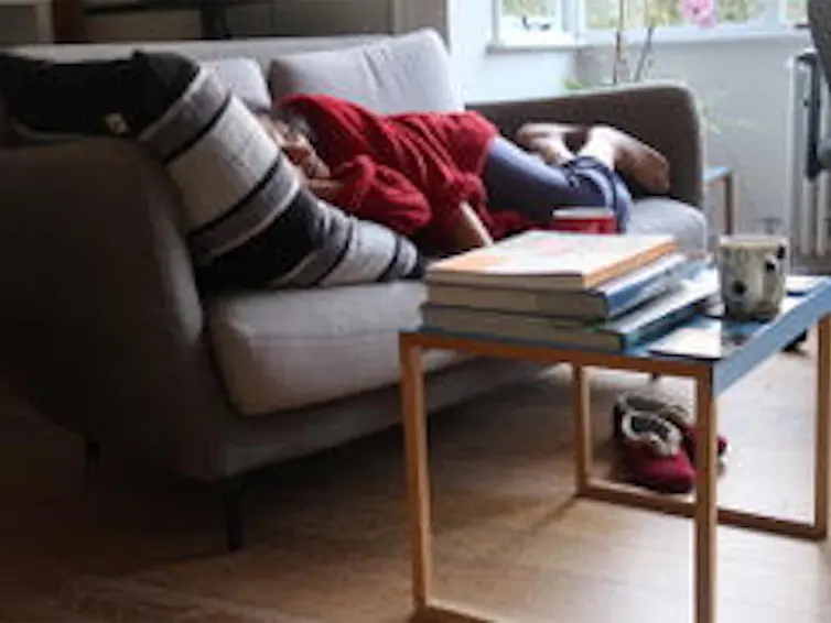 A person sleeping on the sofa under blankets.