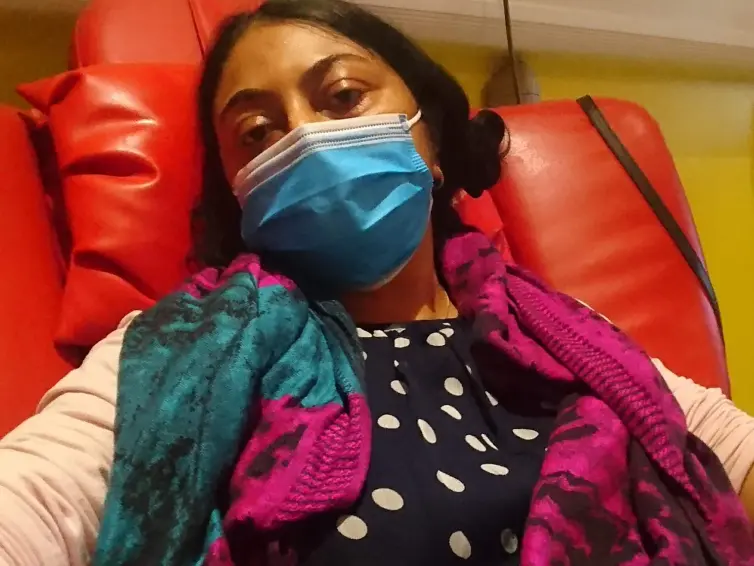 Person looking into camera whilst sitting on a sofa chair receiving drip treatment.