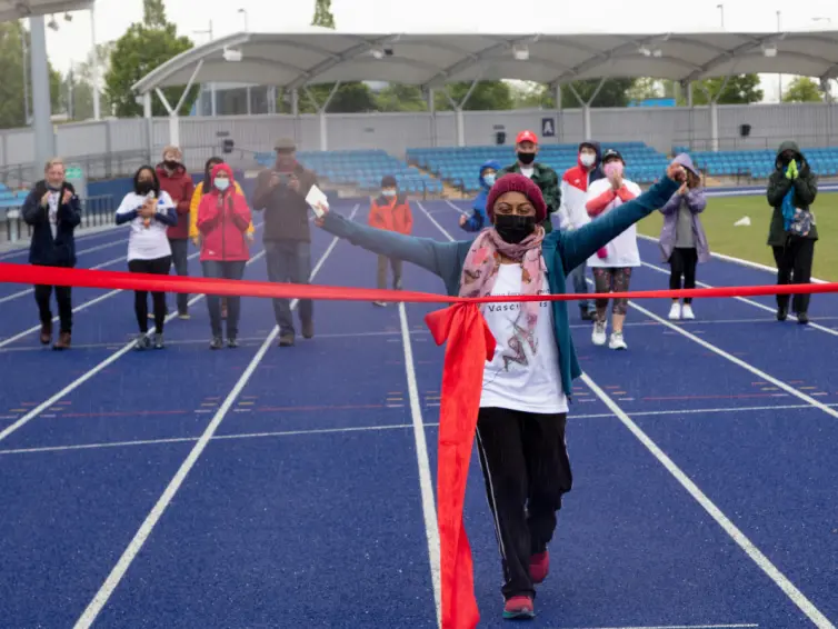 Shanali crossing the finish line of the walking challenge with a smile on her face and arms in the air.