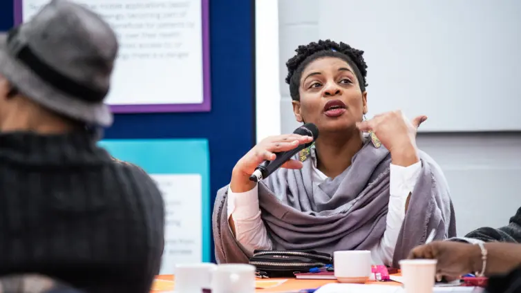 A black female-presenting speaker holding a microphone and talking to people off camera.