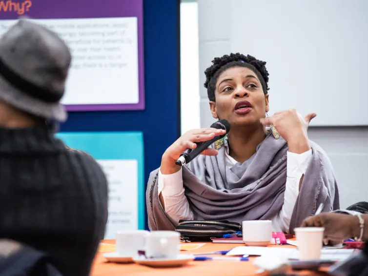 A black female-presenting speaker holding a microphone and talking to people off camera.