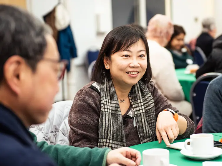 A woman smiling while sitting at a table talking with a group.