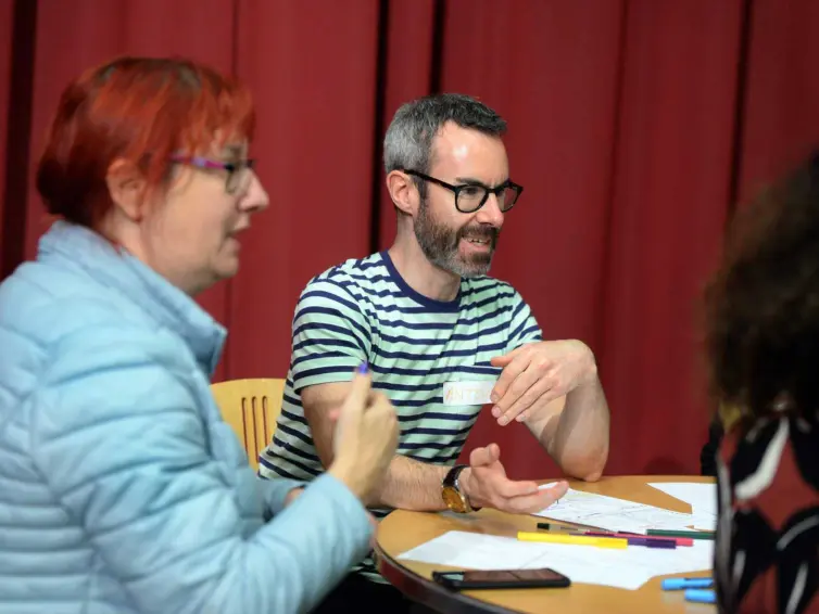 Two people talking with others at a table.