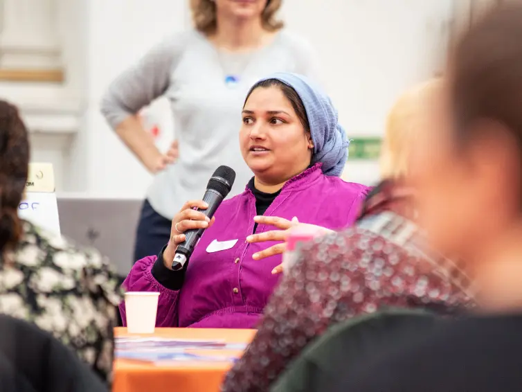 A person wearing a headscarf using a microphone to talk to someone not in the picture frame.