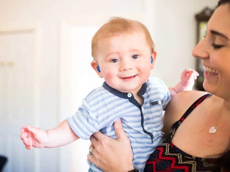 A person holding a smiling baby with hearing aids.