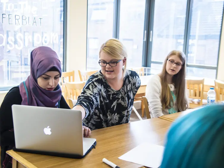 Three people sat at desk looking at laptop.