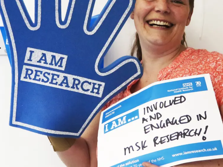 One person holding a sign and a big blue foam hand with 'I am research' written on it.