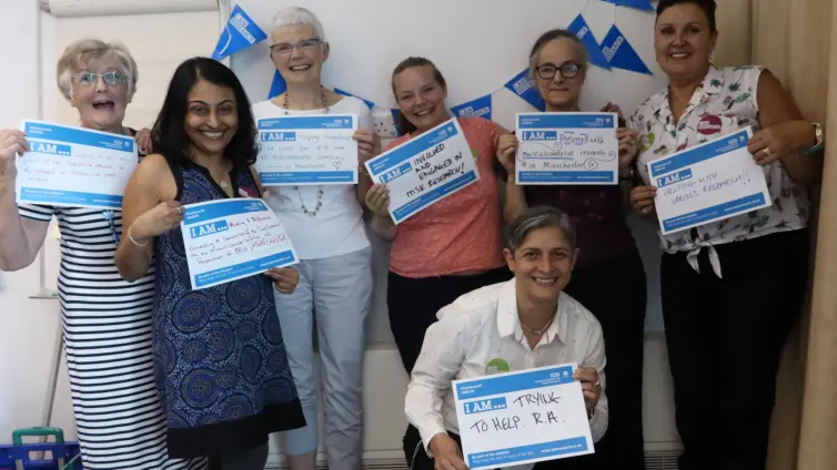 People smiling in one row holding signs 'I am research'.