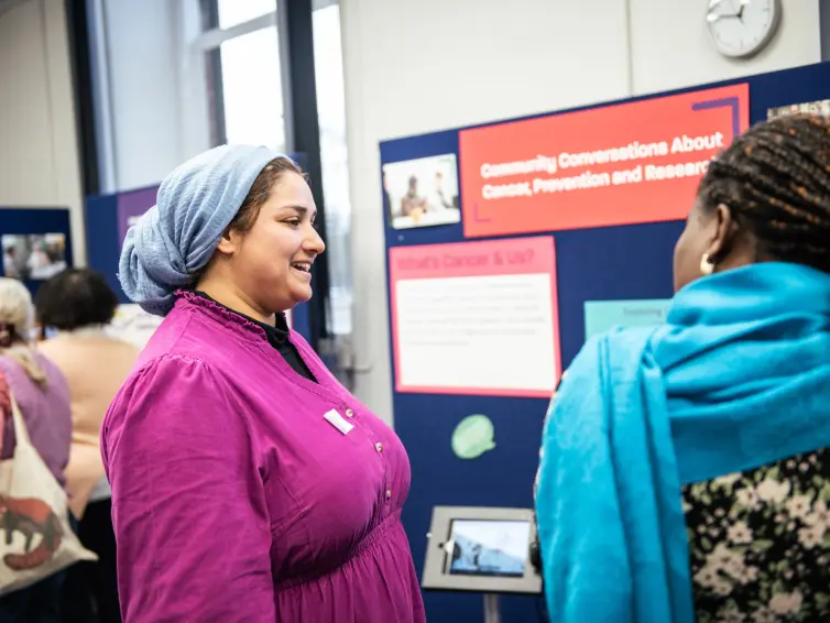 A person looking and smiling at someone else to their right, in the background there are posters about cancer research.