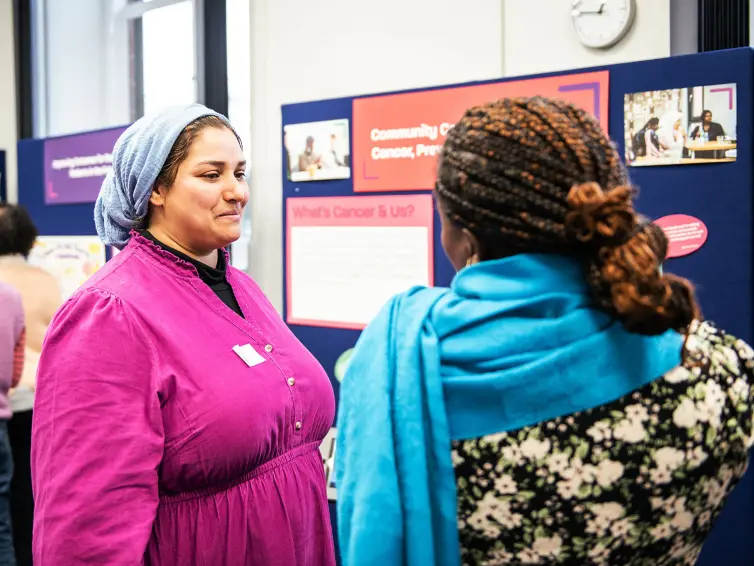 Two people in colourful clothing talking in front of a display board.