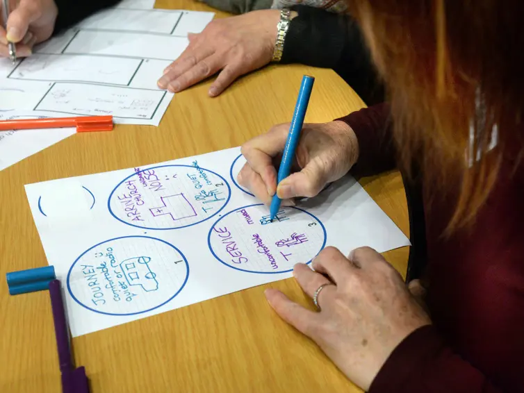 A person participating in a creative activity and writing with a coloured pen on a piece of paper.